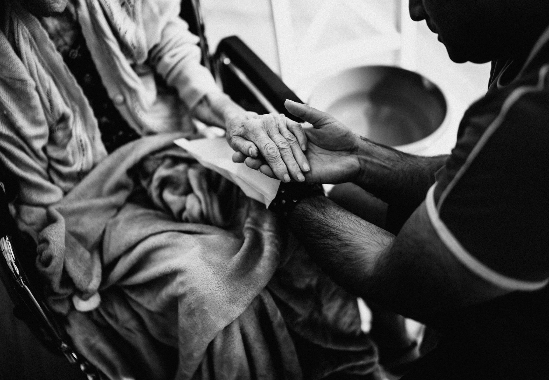 A caregiver holding the hands of an elderly woman in a wheelchair, emphasizing empathy and support.