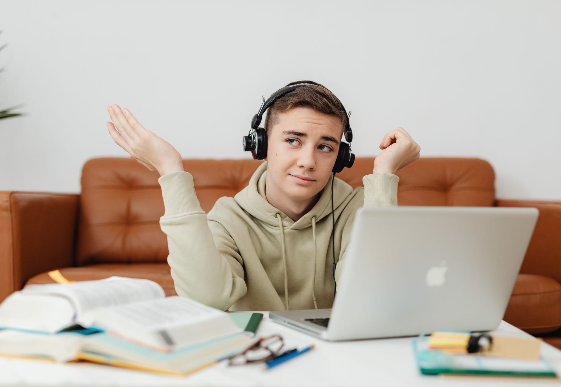 Young man in hoodie using laptop and headphones for online learning at home.