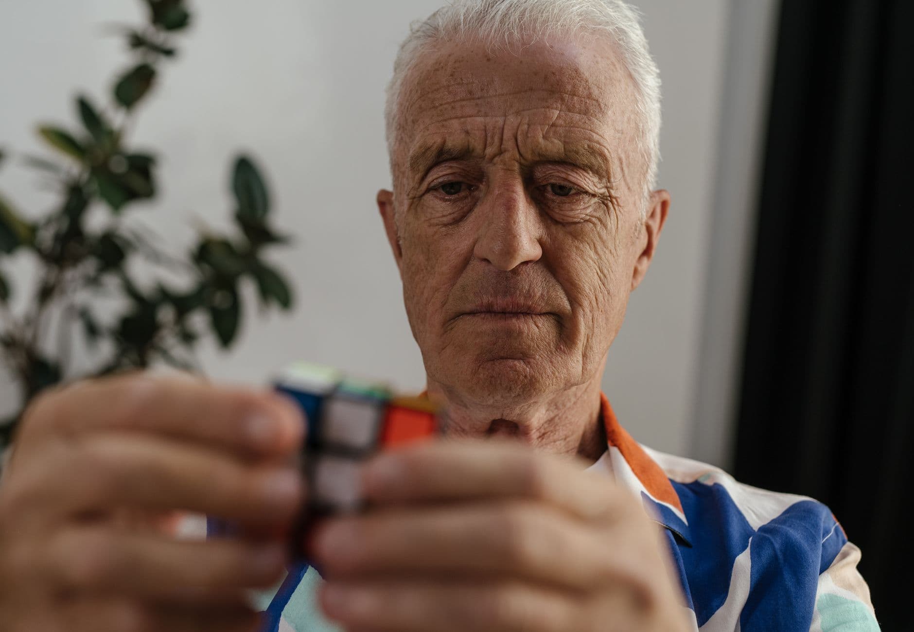 Elderly man concentrating on solving a Rubik's Cube, showcasing focus and mental agility.