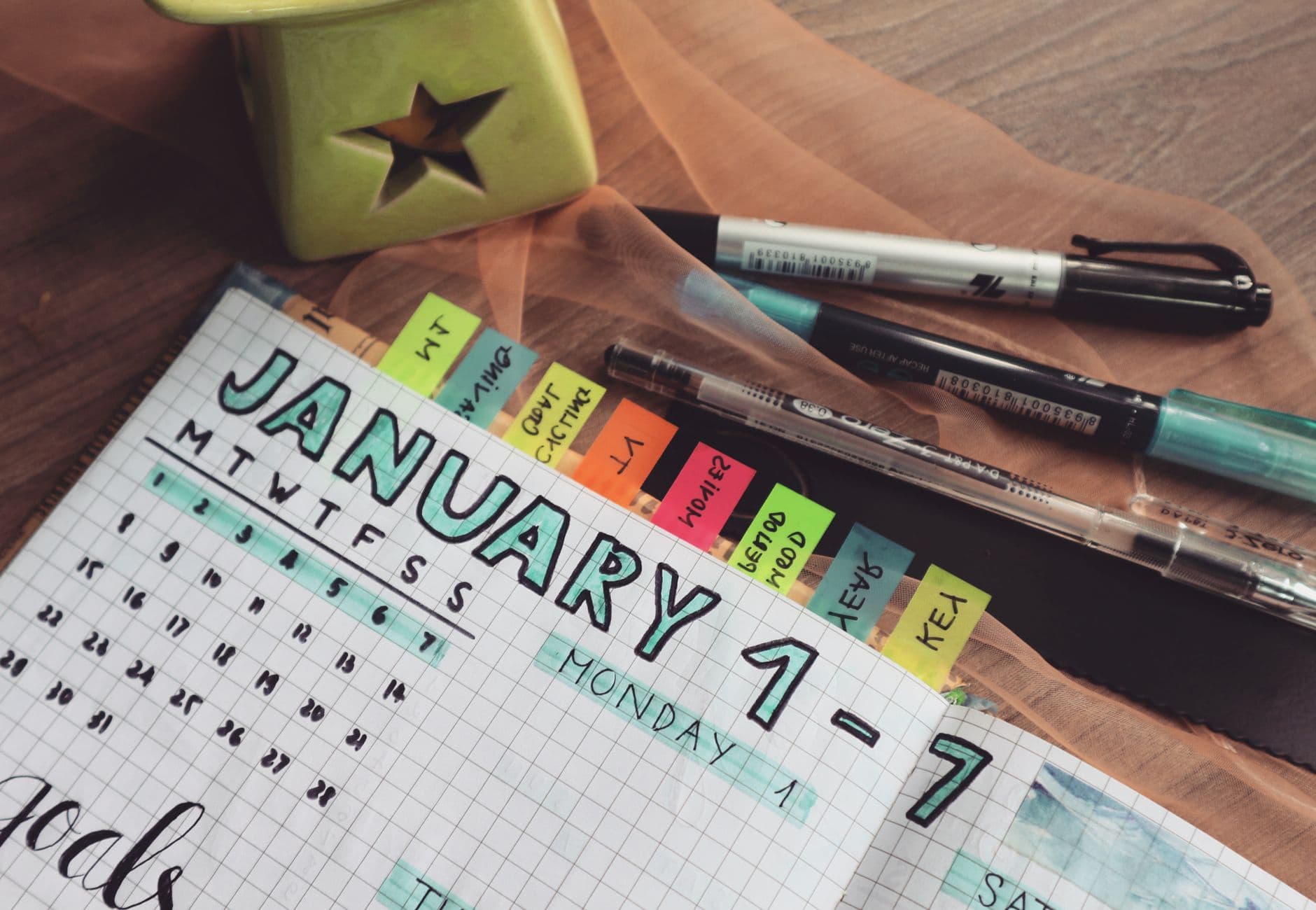 A detailed planner with goals and colorful tabs on a wooden desk with pens.