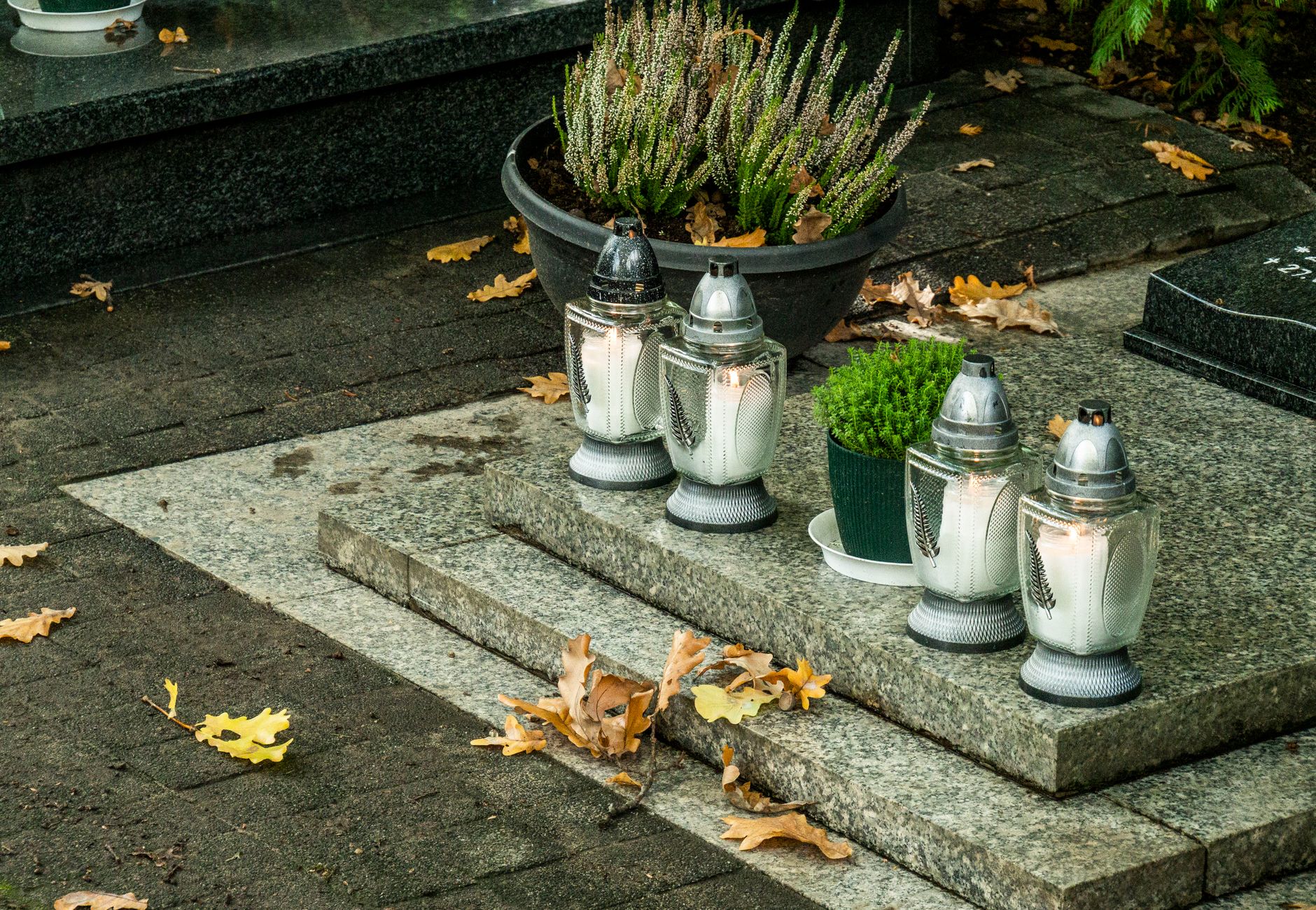 Peaceful cemetery scene with candles and autumn leaves on gravestone.