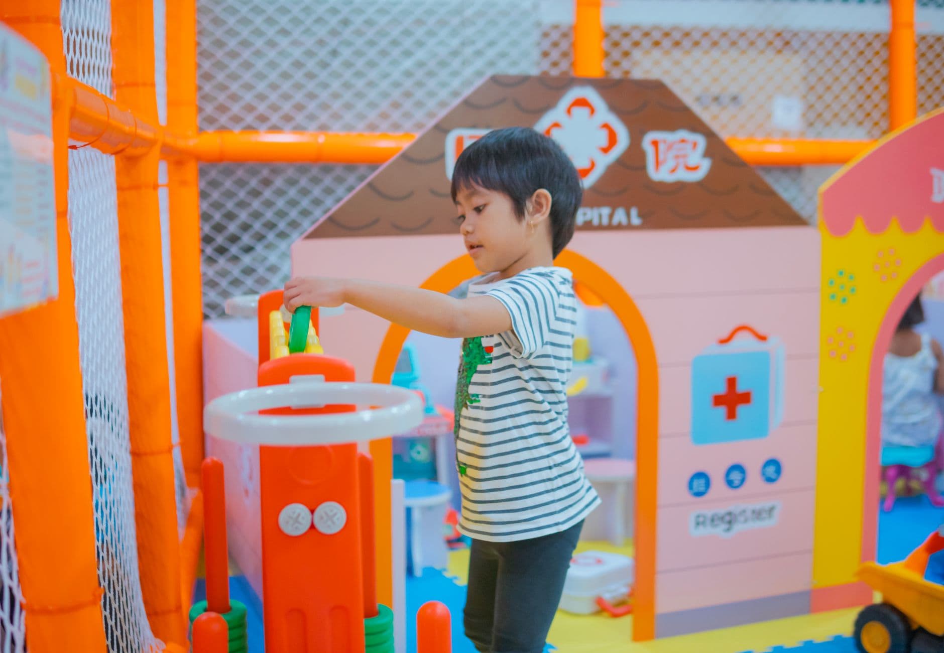 A child enjoys playtime in a colorful indoor playground with toys and structures.