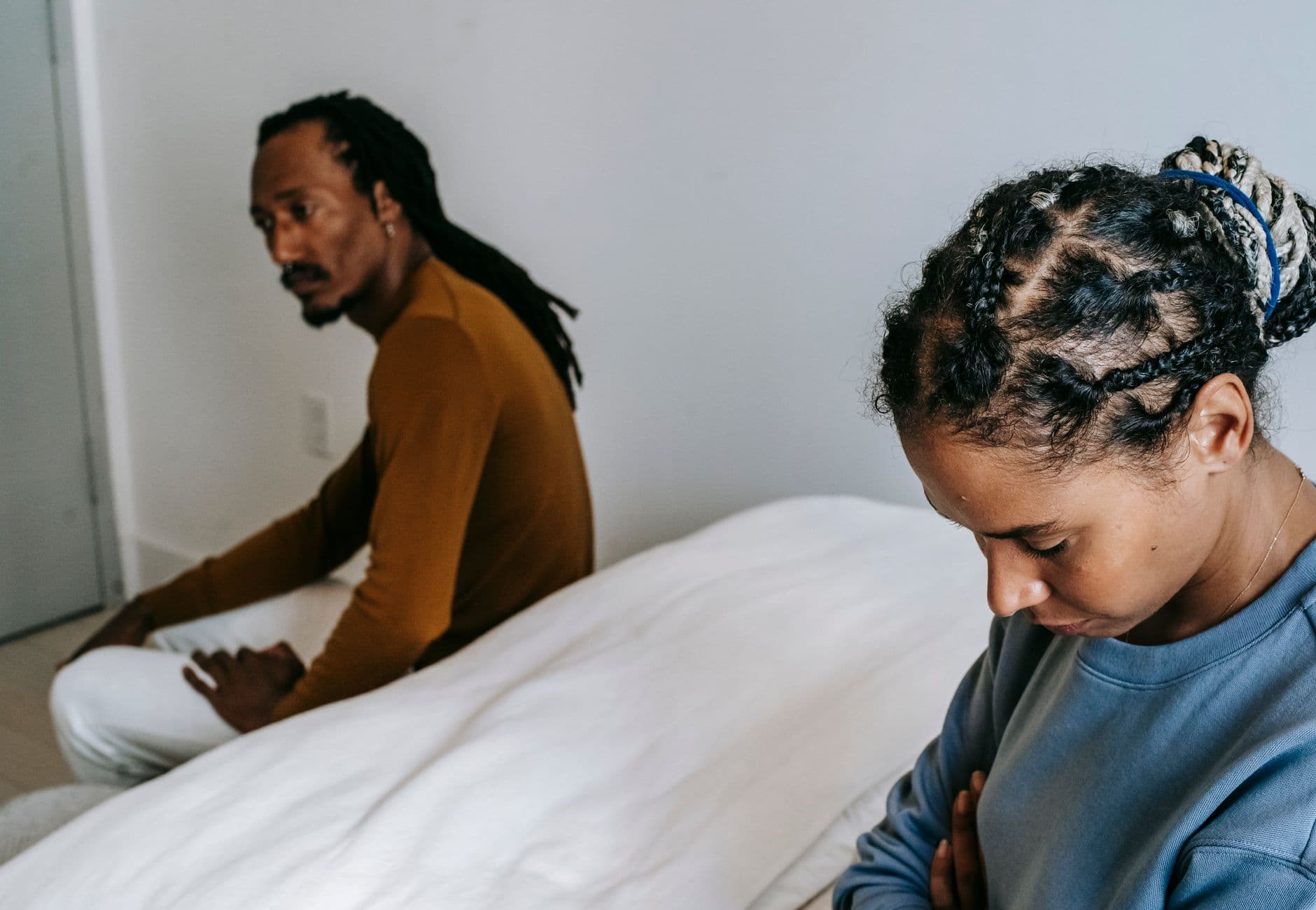 Young black couple in casual outfit sitting on bed with sad face and thinking at home