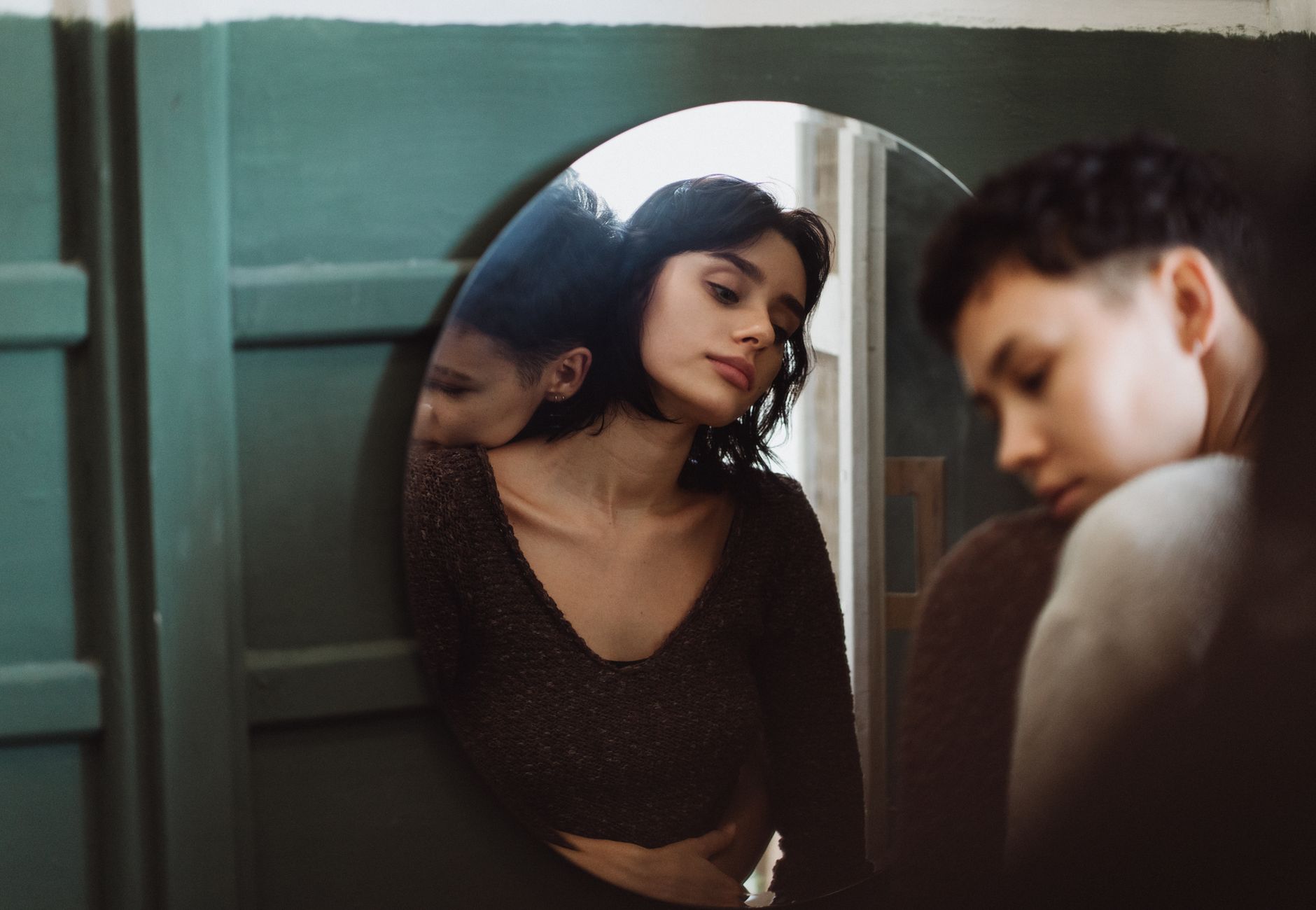 Two people sharing a reflective moment, captured through a mirror in an intimate setting.