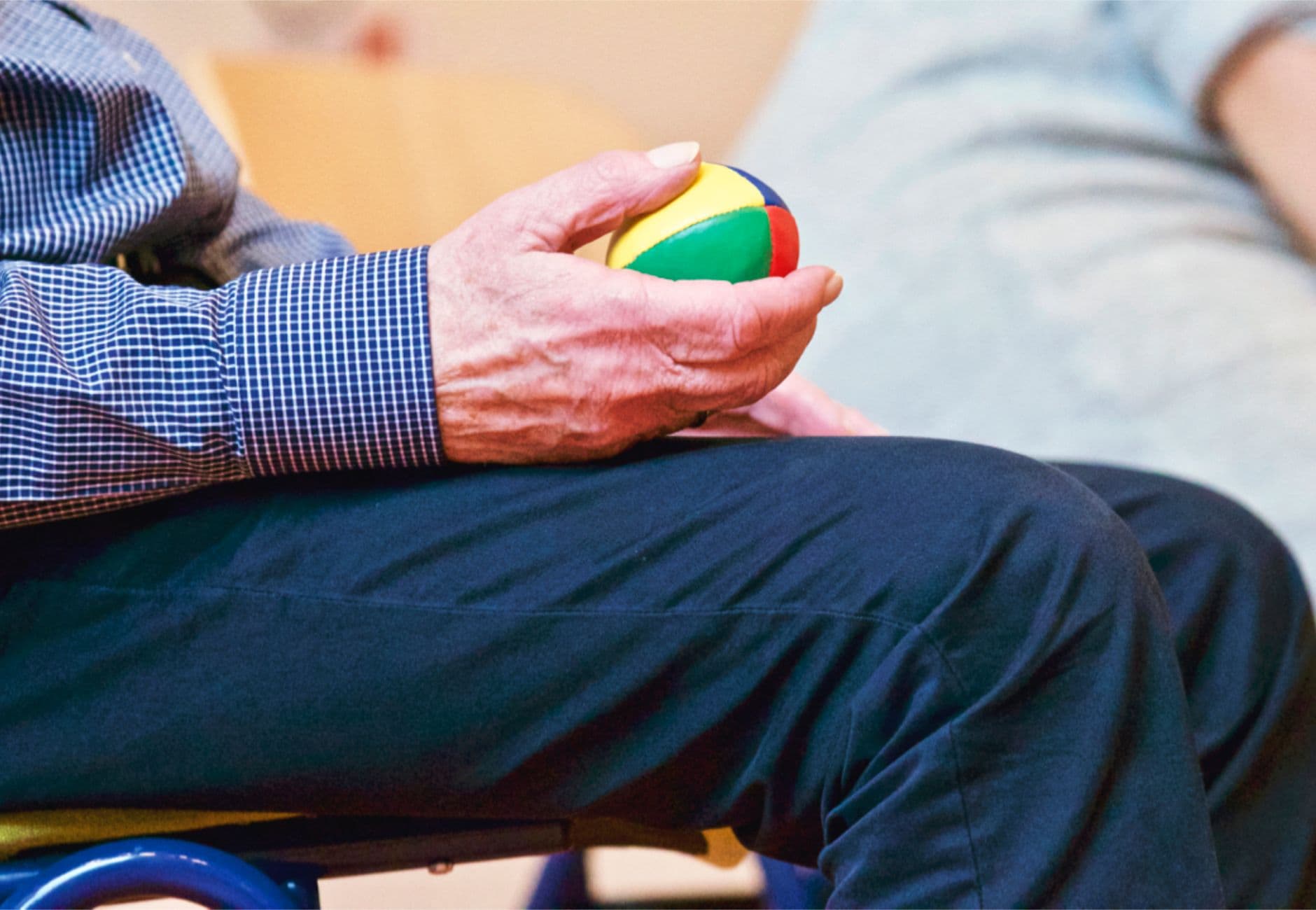 Elderly man holding a colorful therapy ball indoors, promoting relaxation and health.