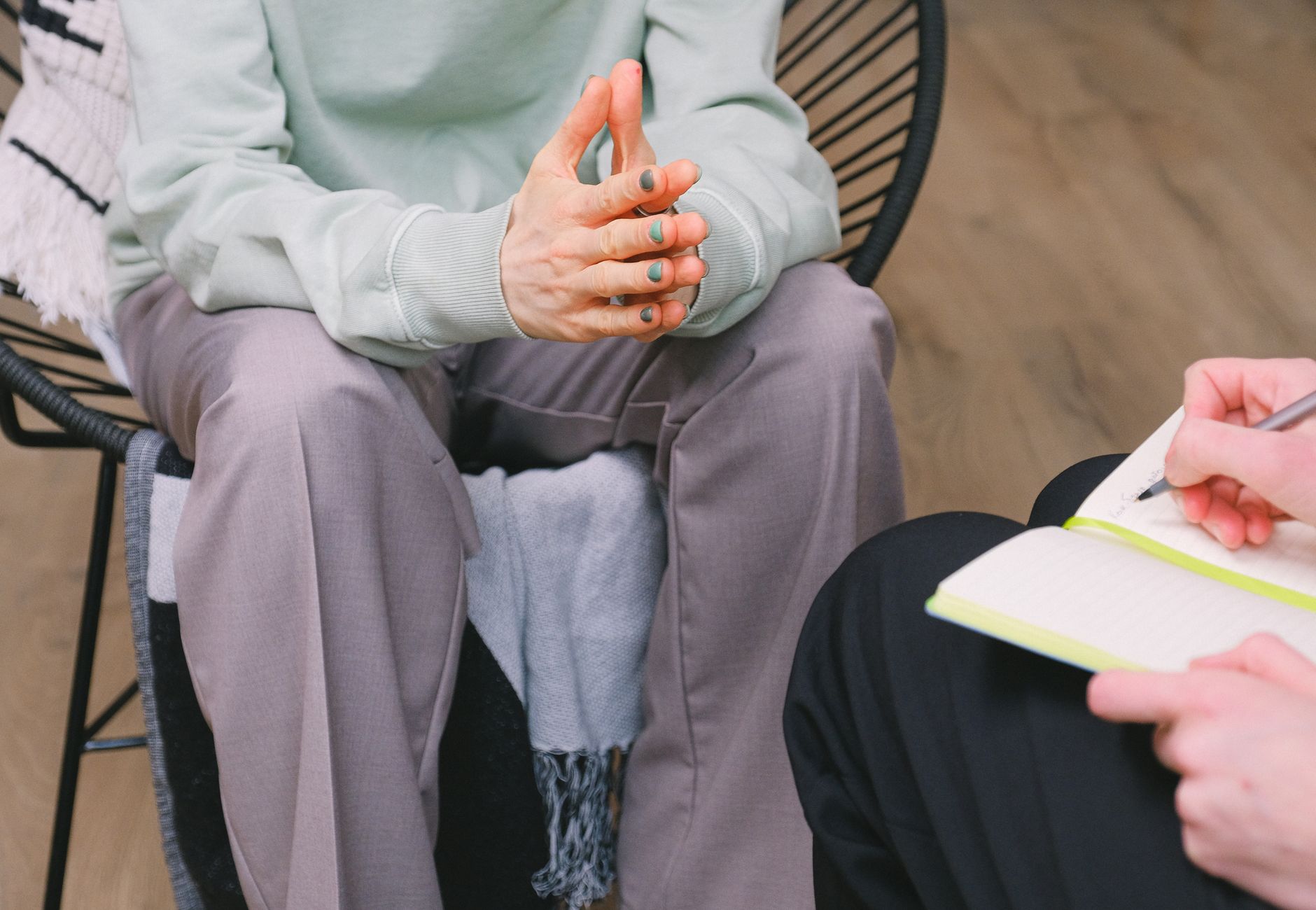 Crop unrecognizable psychotherapist taking notes in journal while interacting with woman on chair during psych